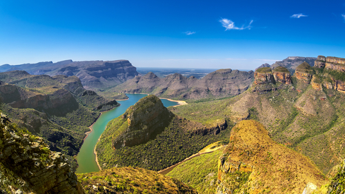 View over a gorge and cliffs with a river running through the middle and the blue sky above.