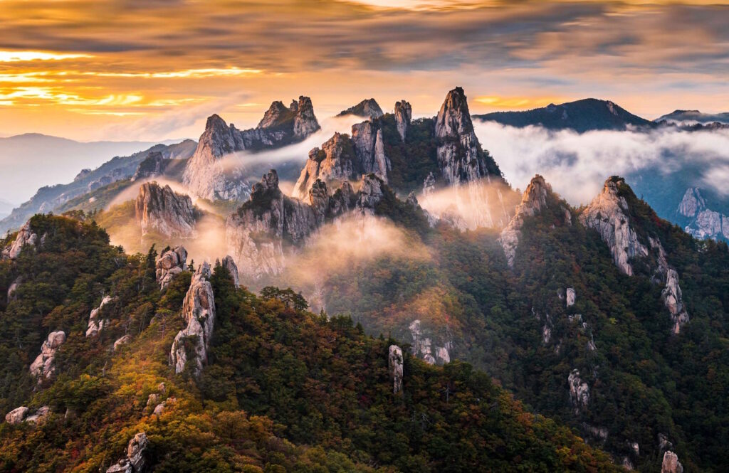 The peaks of Seoraksan National Park draped in clouds and backed by the orange sky of sunset.