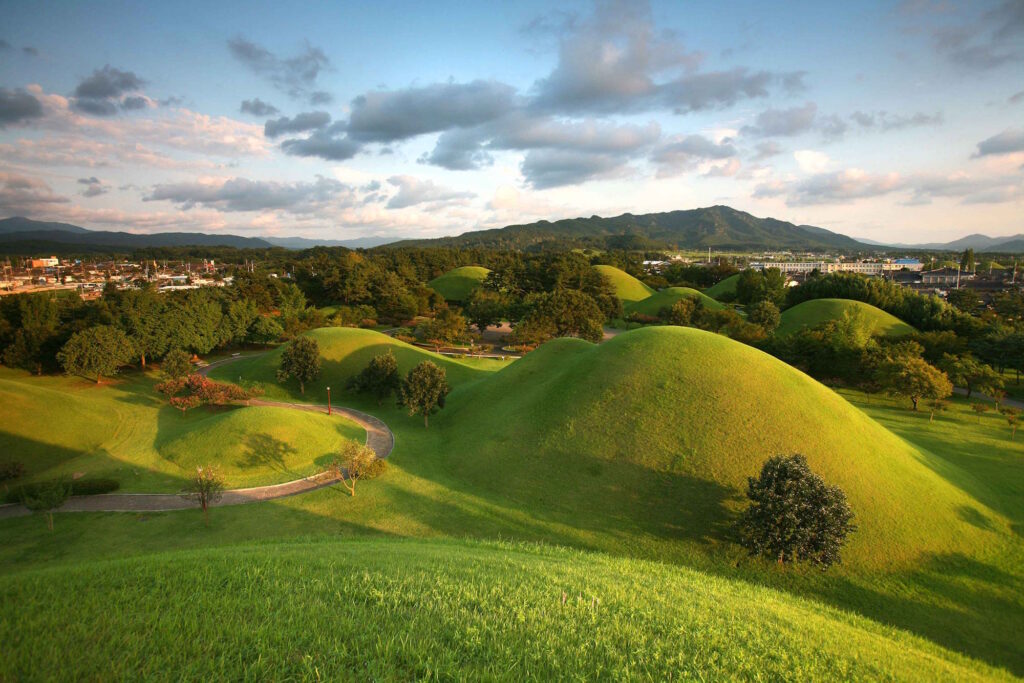 A park filled with grass covered mounds, the ancient tombs of Silla kings and queens, interspersed with trees, and path winding through. 