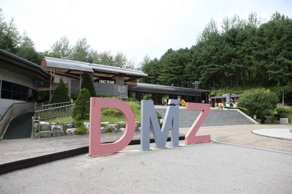 A low building backed by a trees with large letters spelling DMZ in the foreground.