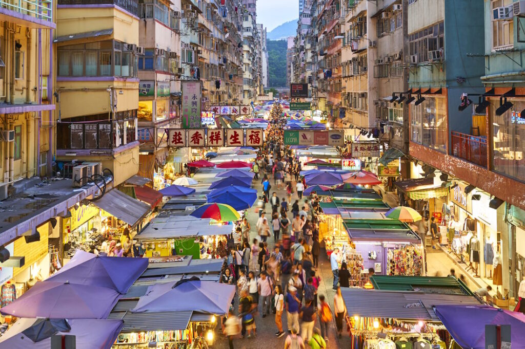 View from above looking along a street of high-rise buildings over the stalls of the busy Mong Kok Ladies Market.