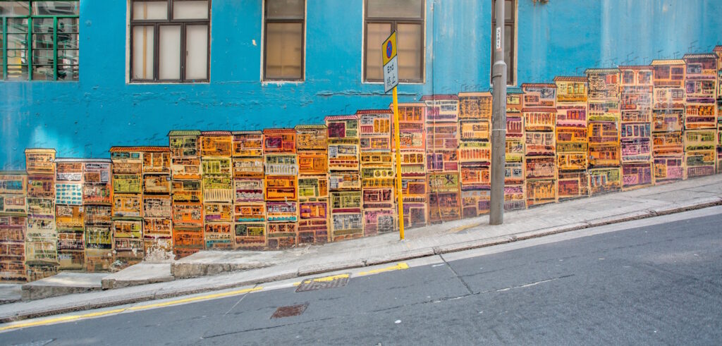 View across a street to street art featuring town houses painted on a blue wall with windows above it