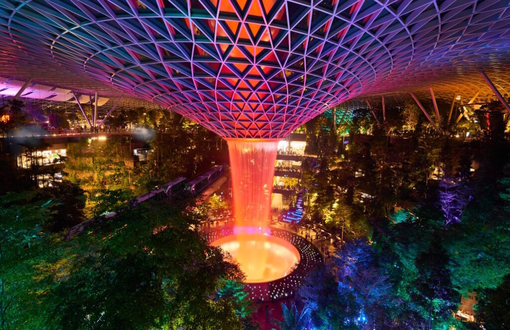 Changi Airport's Rain Vortex lit with colourful lights, by night.