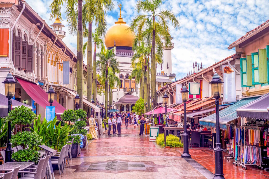 Scenic view of Kampong Gelam, Singapore, featuring the iconic Sultan Mosque with its golden dome, vibrant shophouses, and lush palm trees lining Bussorah Street.